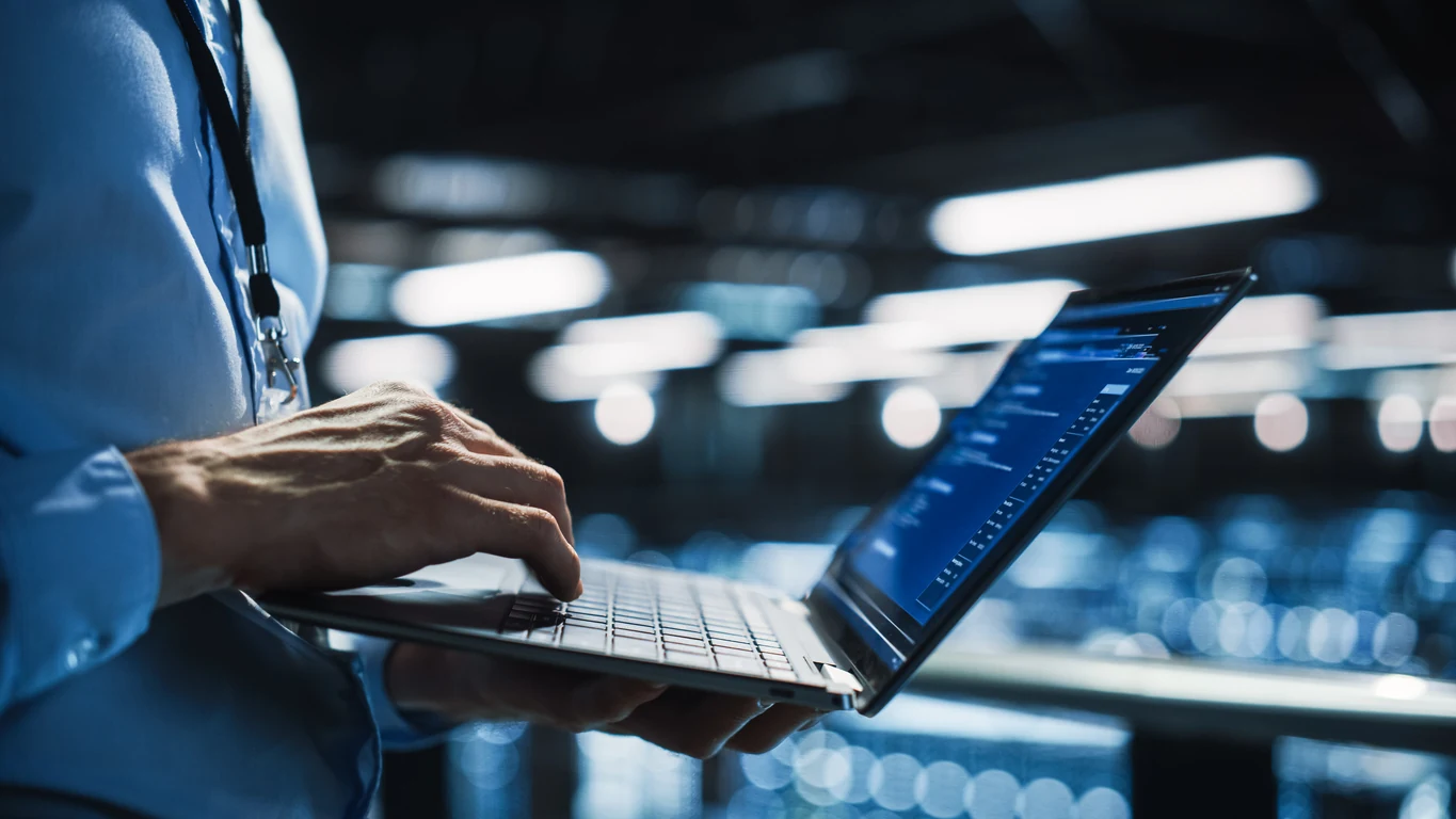 Manos de un especialista con laptop entre racks de un centro de datos